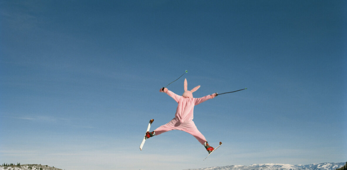 Person wearing pink bunny suit ski jumping, rear view